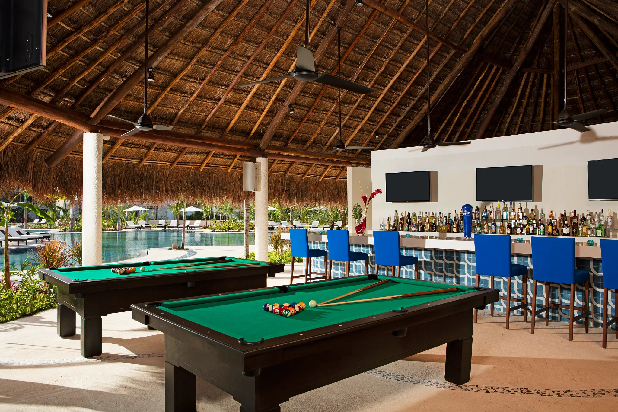 Halftime Bar poolside sports bar at Secrets Akumal Riviera Maya featuring a thatched-roof open-air bar, flat-screen TVs, billiards tables, and pool views.